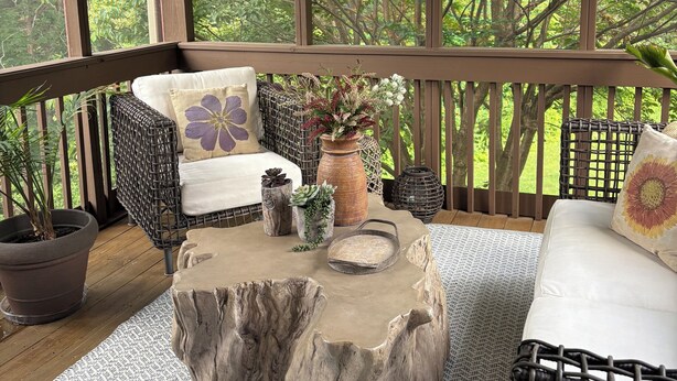 A covered outdoor seating area with wicker furniture, a stone table, and potted plants.