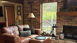A living room with a stone fireplace, leather sofa, and a large window.