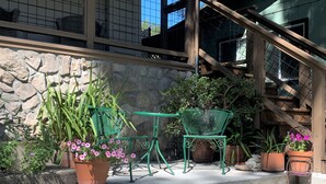 Paret de pedra amb plantes en testos i una cadira de metall verd en un pati.