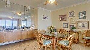 Un coin repas avec des chaises en osier, une table à plateau en verre et un ventilateur de plafond.
