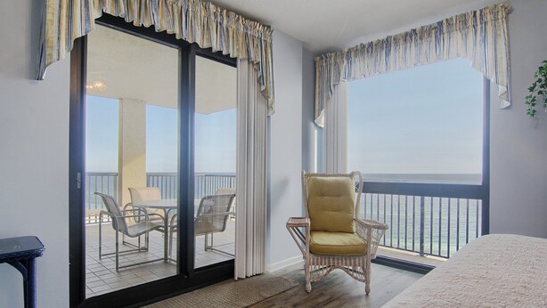 Une chambre dotée d’un grand lit, d’un fauteuil en osier, d’une vue sur le balcon et d’une porte-fenêtre coulissante donnant accès au balcon.