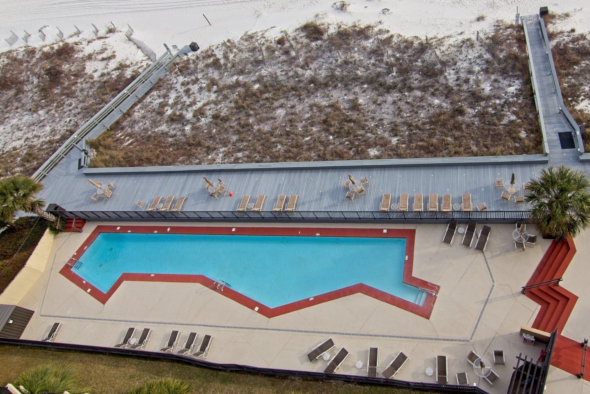 An aerial view of a hotel with a swimming pool, sun loungers, and a beach access ramp.