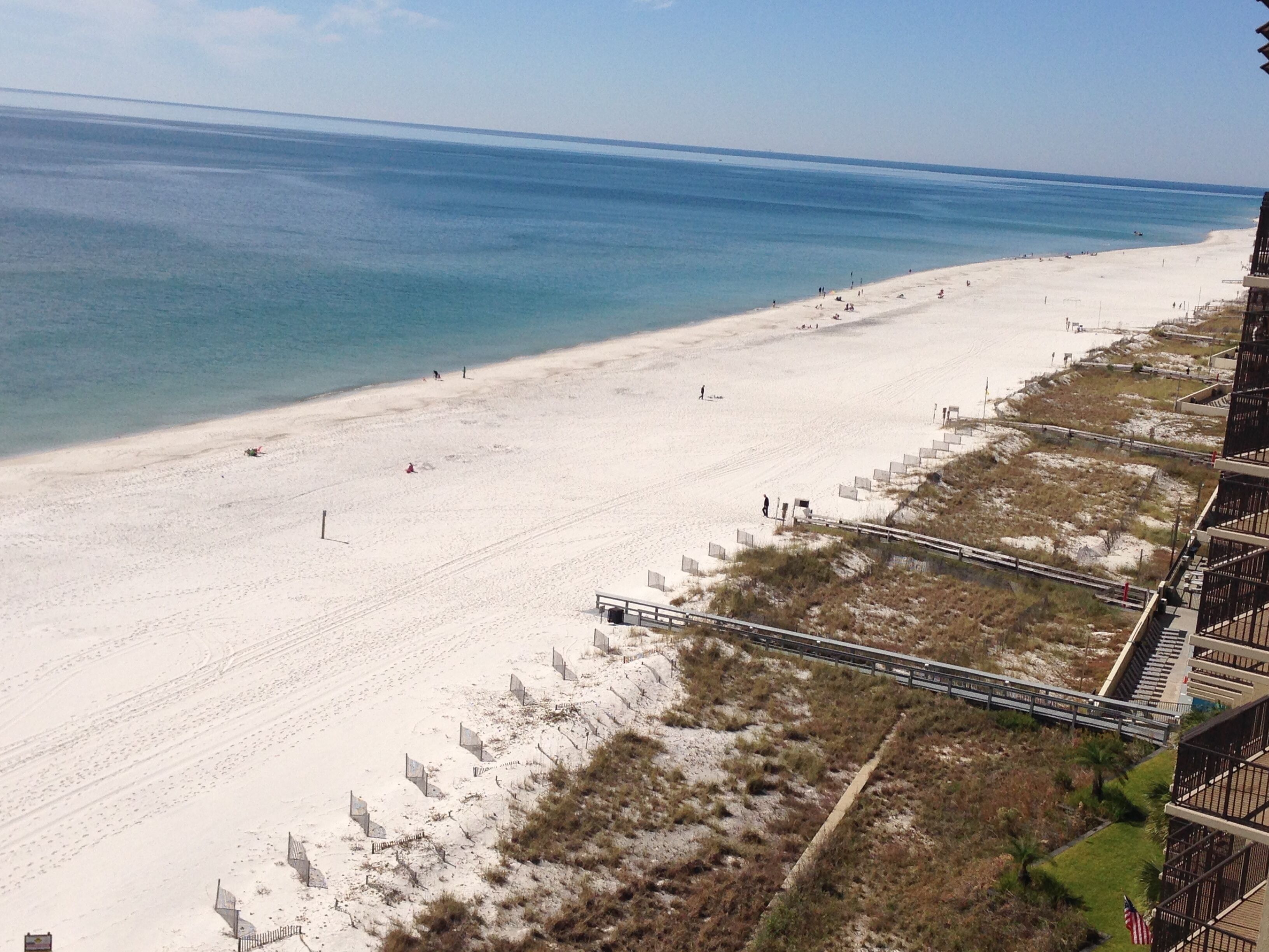A beach with a clear view of the ocean, a sandy shore, and a pedestrian walkway alongside a building.