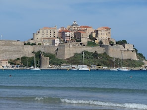 Une ville côtière avec des bâtiments historiques situés sur une colline, un port rempli de bateaux et un ciel dégagé.