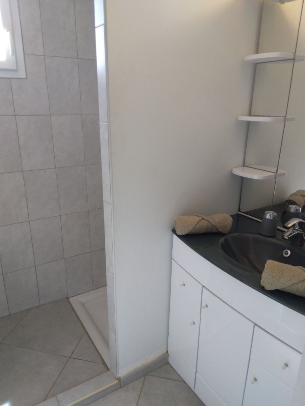 A bathroom with a white vanity, a black sink, and a mirror above it. There are two towels on the sink.