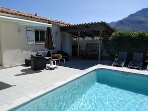 A swimming pool with a tiled deck, outdoor furniture, and a pergola.