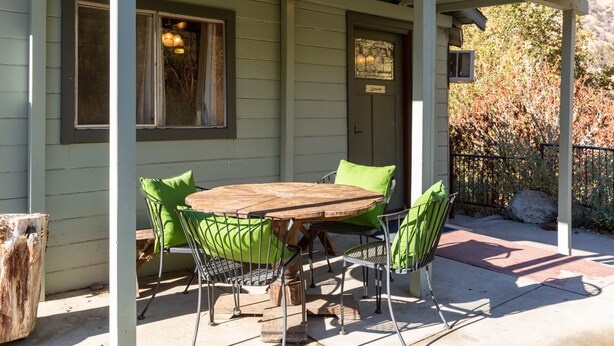 A covered patio with a wooden table and four chairs, a wooden post, and a metal railing.
