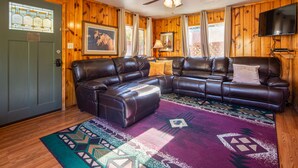 A cozy living room with a sectional sofa, a ceiling fan, and a large window with curtains.