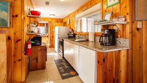 A wooden cabin kitchen with a refrigerator, stove, coffee maker, and a fire extinguisher.