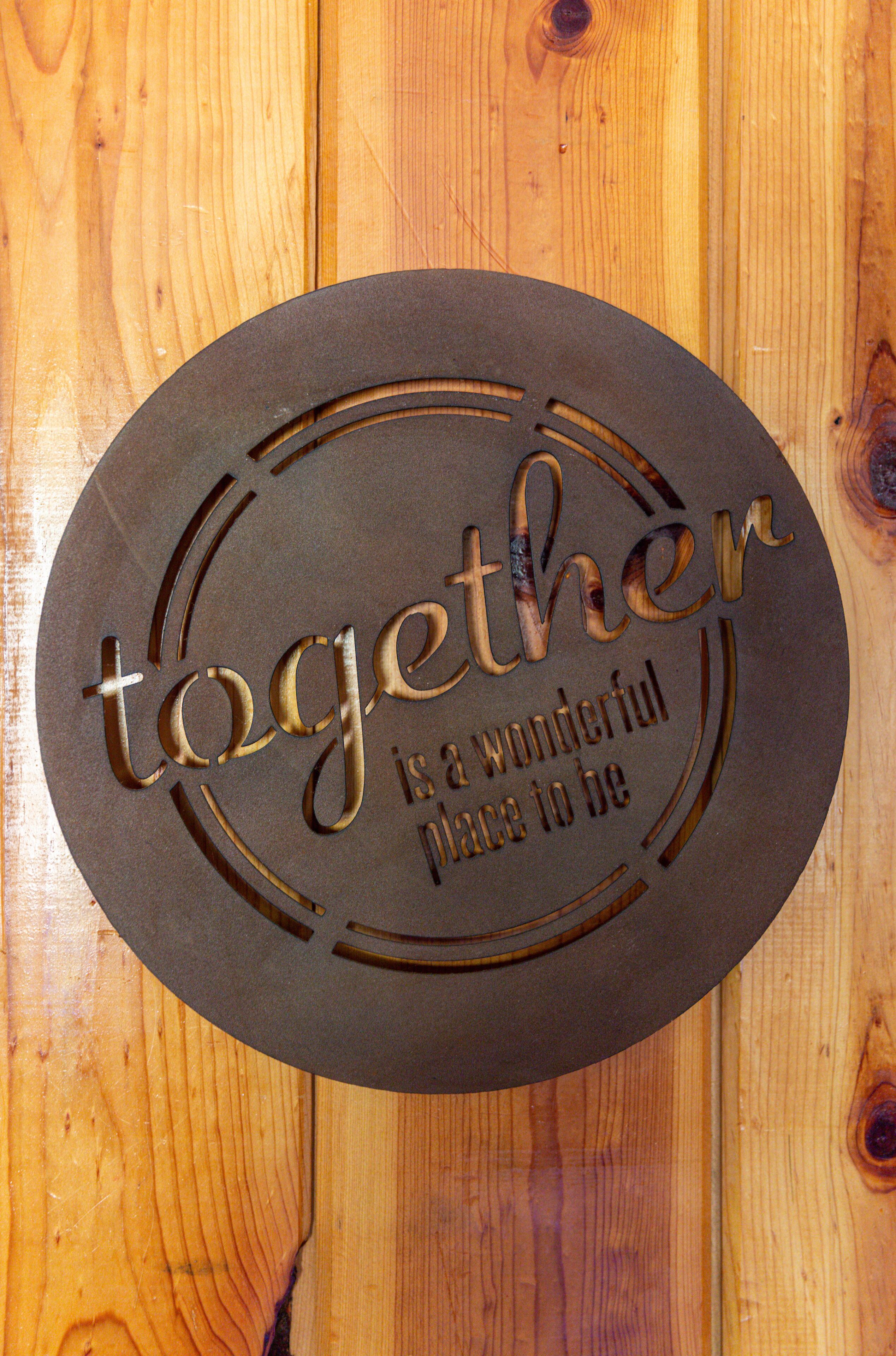 A circular wooden plaque with the words "Together is a wonderful place to be" engraved on it.