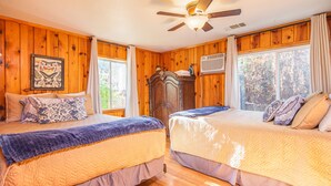 A room with two beds, wooden walls, a ceiling fan, and a window with curtains.