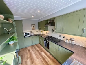 A modern kitchen with green cabinets, a microwave, a gas stove, and a sink.