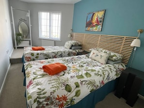 A bedroom with two beds, a window with blinds, a painting on the wall, and a bedside lamp.