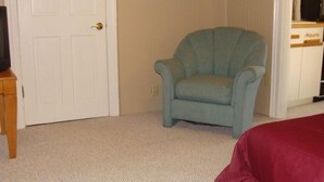 A room with a teal armchair, a wooden side table, a white door, and a kitchenette area with cabinets and a microwave. - Cozy studio in St. Joseph, Michigan (St Joseph)