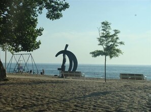 Une plage agrémentée d’une grande sculpture abstraite, d’une balançoire et de quelques bancs.