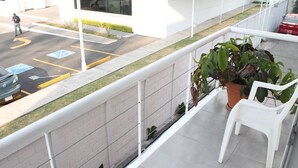 A balcony with a potted plant and a white chair, overlooking a parking area with marked spaces and a building in the background.