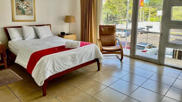 A hotel room with a bed, a chair, a lamp, and a view of the street through a glass door.