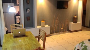A dining area with a wooden table, chairs, a laptop, and a TV mounted on the wall.