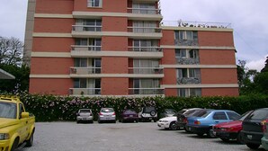 A multi-story apartment building with balconies, a parking lot, and a variety of parked cars.