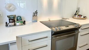 A modern kitchen with a built-in stove, stainless steel cabinets, and a range hood. - The Pop Hauz - Large Pool House (Naples)