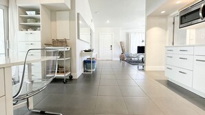 A modern kitchen with white cabinetry, a stainless steel range hood, and a clear glass chair. - The Pop Hauz - Large Pool House (Naples)