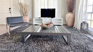 A living room with a TV, a sofa, a coffee table, and decorative plants. - The Pop Hauz - Large Pool House (Naples)