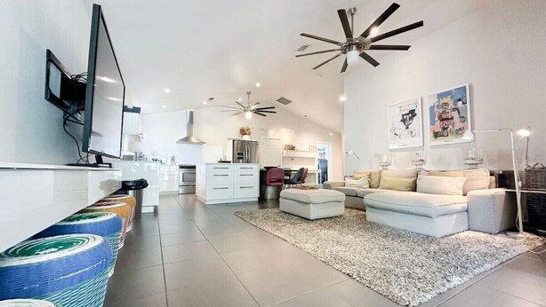 A modern living room with a sofa set, a coffee table, a TV mounted on the wall, and a kitchen area in the background. - The Pop Hauz - Large Pool House (Naples)