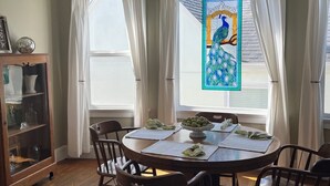 Ein Esszimmer mit einem runden Tisch, sechs Stühlen, einer Chandelier und einem Buntglasfenster mit Pfauenmotiv.