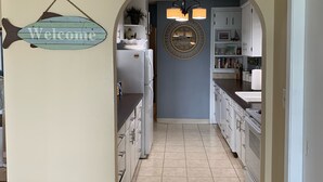 Una cocina con armarios blancos, un letrero de bienvenida, un reloj y una araña.
