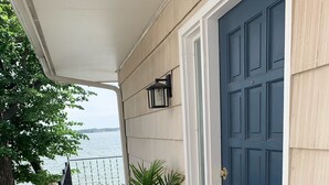 Una terraza de madera con una puerta azul, una planta amarilla en maceta y un felpudo con diseño de piña.