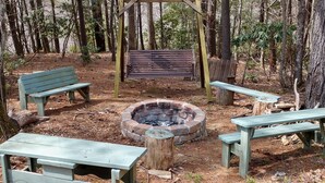 A forested campsite with a fire pit, benches, and picnic tables. - The Secluded Hideaway (West Jefferson)