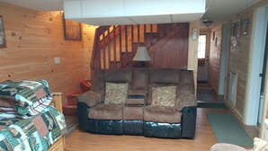 A cozy cabin interior with a wooden staircase, a leather recliner with cushions, a wooden chest of drawers, and a patterned blanket on a couch. - The Secluded Hideaway (West Jefferson)