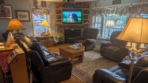 A cozy living room with a fireplace, leather sofas, a television, and a large window with curtains. - The Secluded Hideaway (West Jefferson)