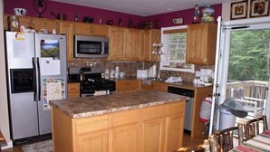 A kitchen with wooden cabinets, a refrigerator, microwave, stove, and a dining area with a table and chairs. - The Secluded Hideaway (West Jefferson)