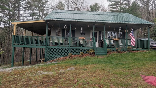 A rustic cabin with a green metal roof, a porch with a green railing, and an American flag. - The Secluded Hideaway (West Jefferson)