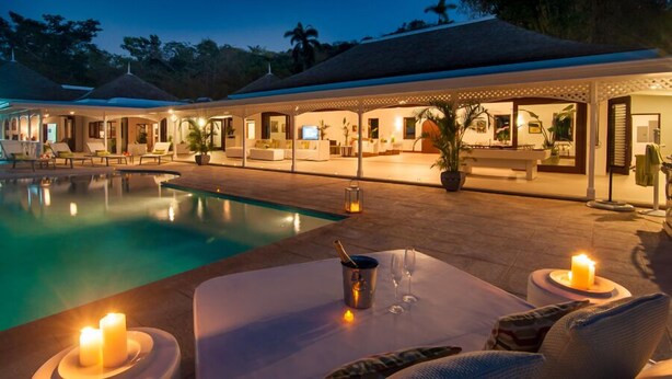 Un espace aménagé au bord de la piscine, avec des chaises longues, une table décorée de bougies et un coin bar équipé d’un téléviseur.