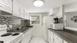 Una cocina compacta con armarios blancos, un salpicadero de azulejos blanco y negro, un refrigerador blanco y un microondas.