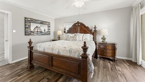Un dormitorio con una cama grande, una mesita de noche, un aparador, un ventilador de techo y una obra de arte colgada en la pared.