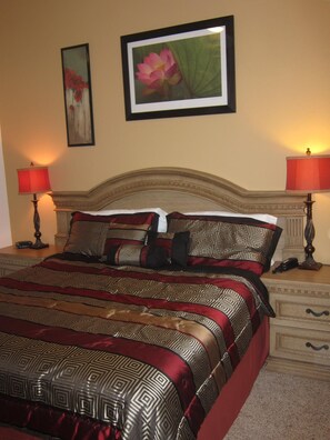 A hotel room with a large bed, two bedside tables, a headboard, and two lamps.