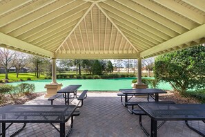 A covered outdoor area with picnic tables and a view of a golf course.