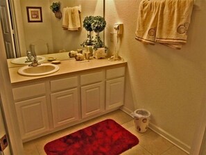A bathroom with a beige vanity, two sinks, a red rug, and a trash can.