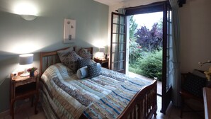 Ein Schlafzimmer mit einem Bett, Nachttischen, Vorhängen an einem Fenster und Blick auf Grünfläche.