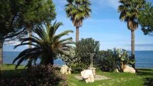A garden with palm trees, a pathway, and a view of the sea. - Apartment on the beach in Baia dei Turchi- 6/7 persons (Brucoli)