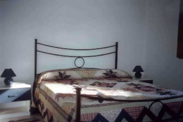 A single bed with a metal frame, a patterned bedspread, and two bedside lamps on matching nightstands.