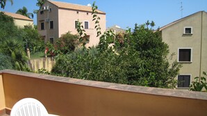A balcony with a white chair, surrounded by lush greenery and buildings in the background. - Apartment on the beach in Baia dei Turchi- 6/7 persons (Brucoli)