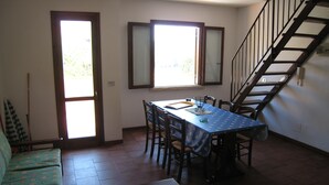 A dining area with a table and chairs, a sofa, and a staircase. - Apartment on the beach in Baia dei Turchi- 6/7 persons (Brucoli)