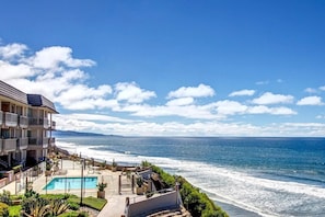 A beachfront hotel with a swimming pool, outdoor seating, and ocean views.