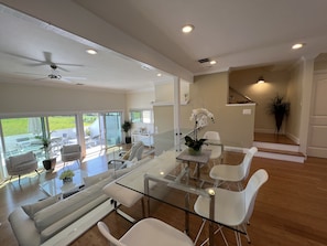 A modern living room with a glass coffee table, white sofas, and a view of the outdoors.