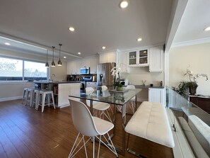 A modern kitchen with white cabinetry, a glass dining table, and bar stools.