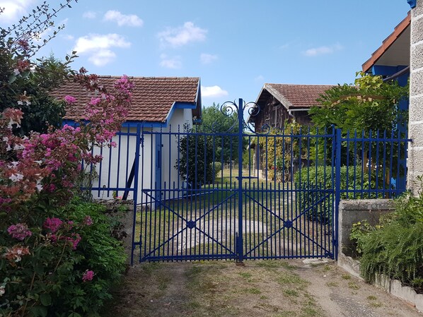 Una entrada protegida con un portón azul, rodeada de abundante follaje y plantas con flores.